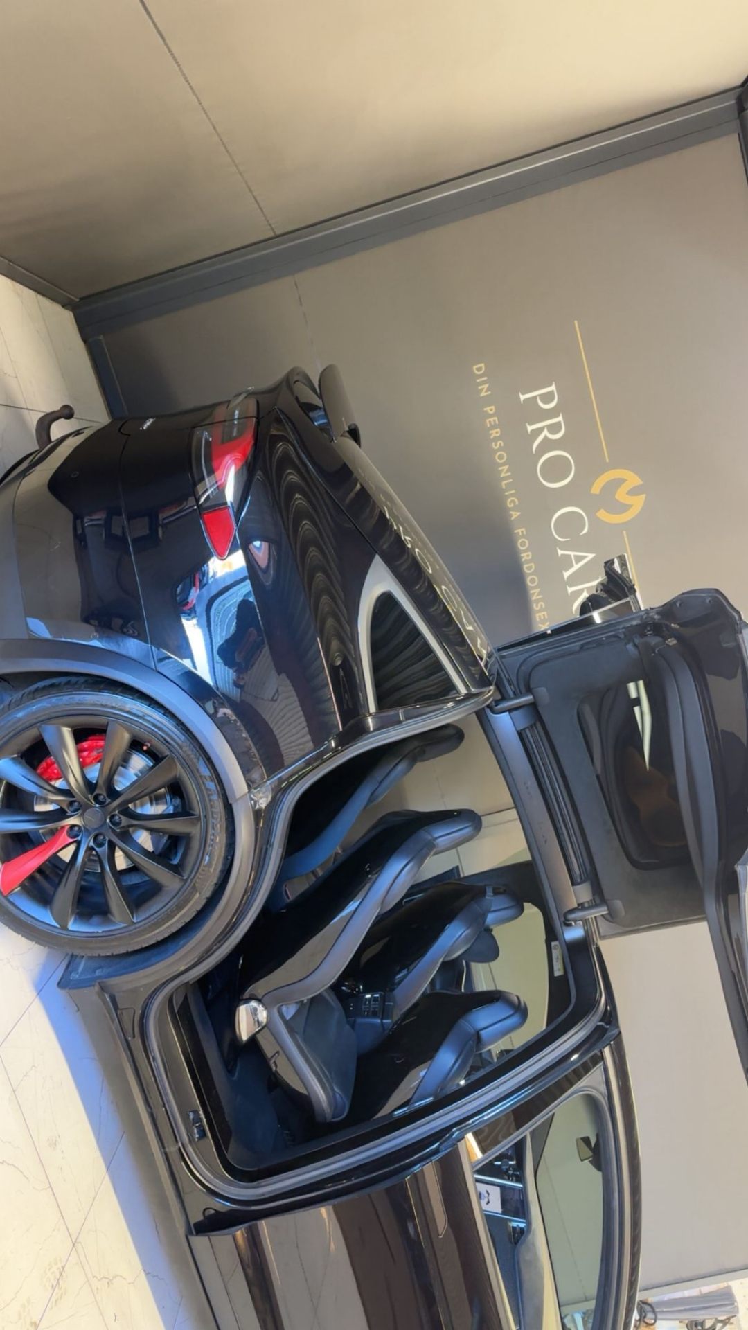 Svart Tesla Model X med öppen dörr framför Pro Cars logotyp i showroomet